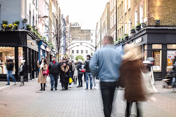 People walking own a typical London pedestrianised high street with shops either side.